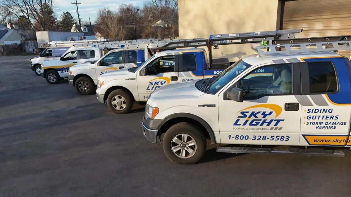 The Skylight Roofing truck fleet lined up outside the shop, each one signwritten for roofing, siding, gutters and storm damage repairs