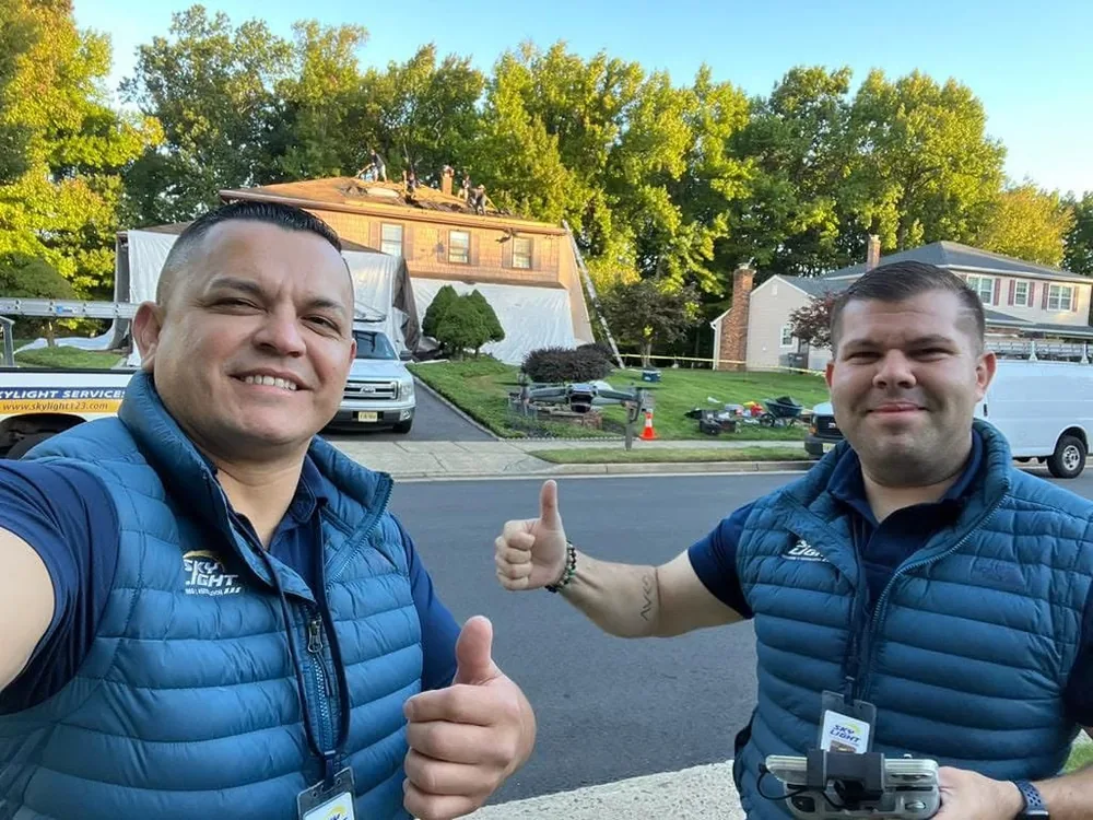 Two Skylight Roofing estimators outside a New Jersey home with the roof stripped and the crew laying new underlayment