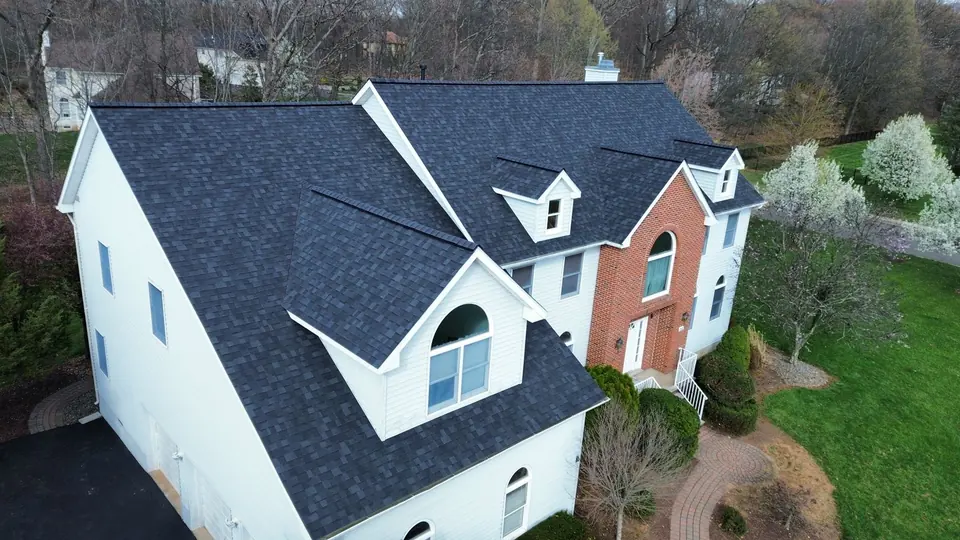 Dark charcoal shingle roof on a white two story home, photographed from the air after replacement