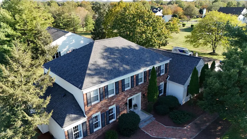Dark shingle roof replacement on a brick home surrounded by mature trees