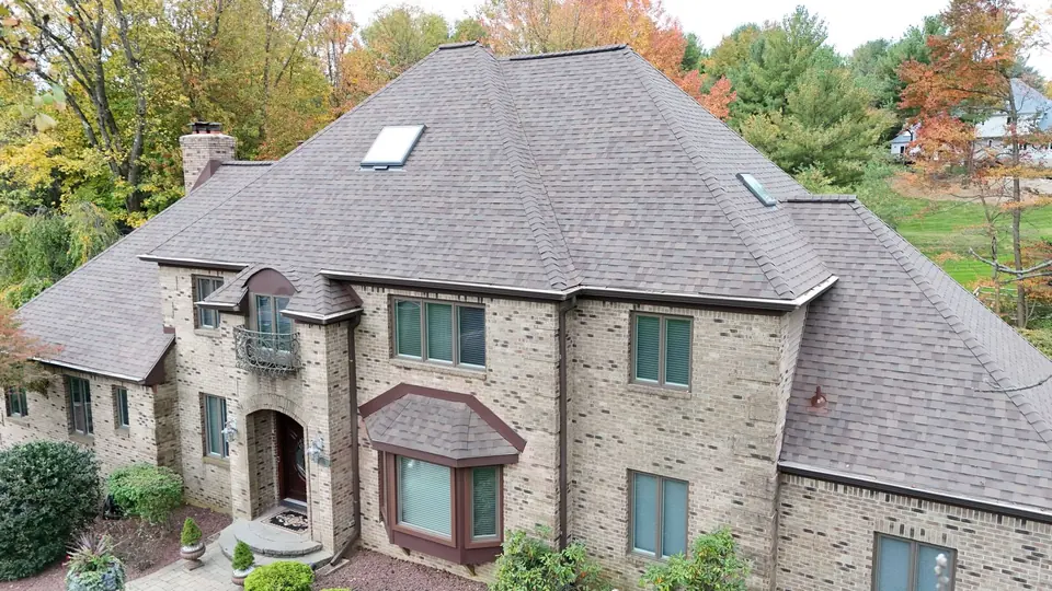 Large stone home with a new gray shingle roof and skylight, seen from above