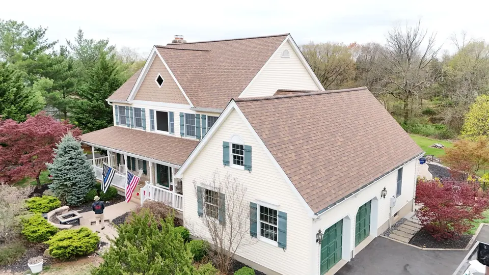 Newly shingled roof on a cream sided home with dormers and mature landscaping