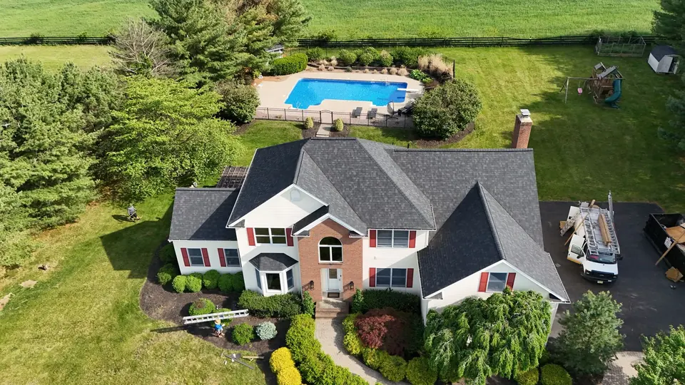 New roof on a home with red shutters and a backyard pool, aerial view