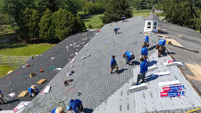 Skylight Roofing crew laying synthetic underlayment and shingles across a large roof, seen from the air