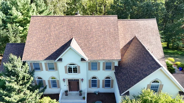 Completed shingle roof with steep gables on a cream stucco colonial home, front aerial view