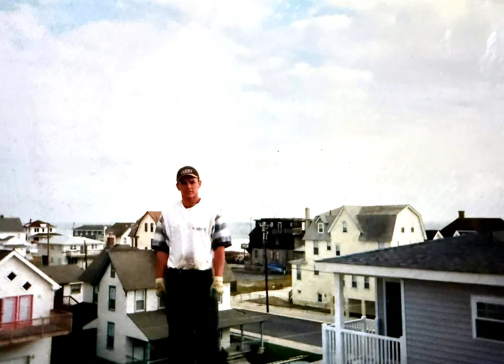 A young Mauricio Saenz standing on a roof above a street of houses packed close together