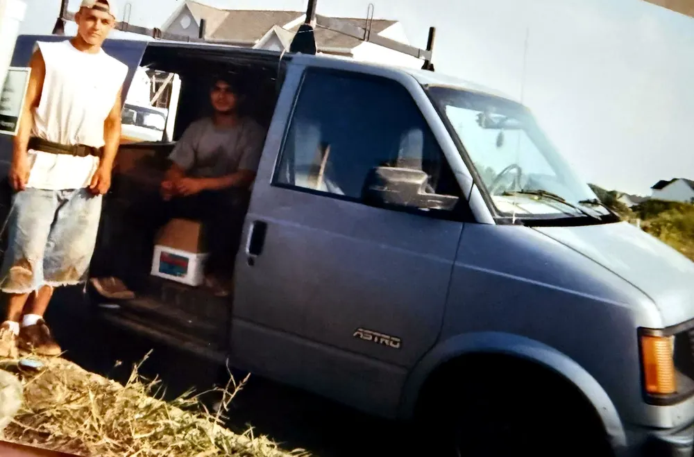 Mauricio Saenz and a crewmate early in his career, beside a Chevrolet Astro work van loaded with roofing gear, ladder rack on top